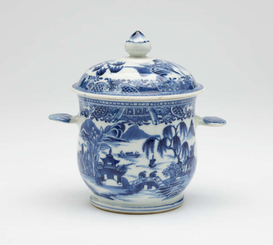 A white bowl with flat handles and lid. The blue decorations are architectural and floral.