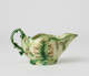  A short boat shaped pitcher green, cream, and brown in color with a sculptural handle and floral decorations.
