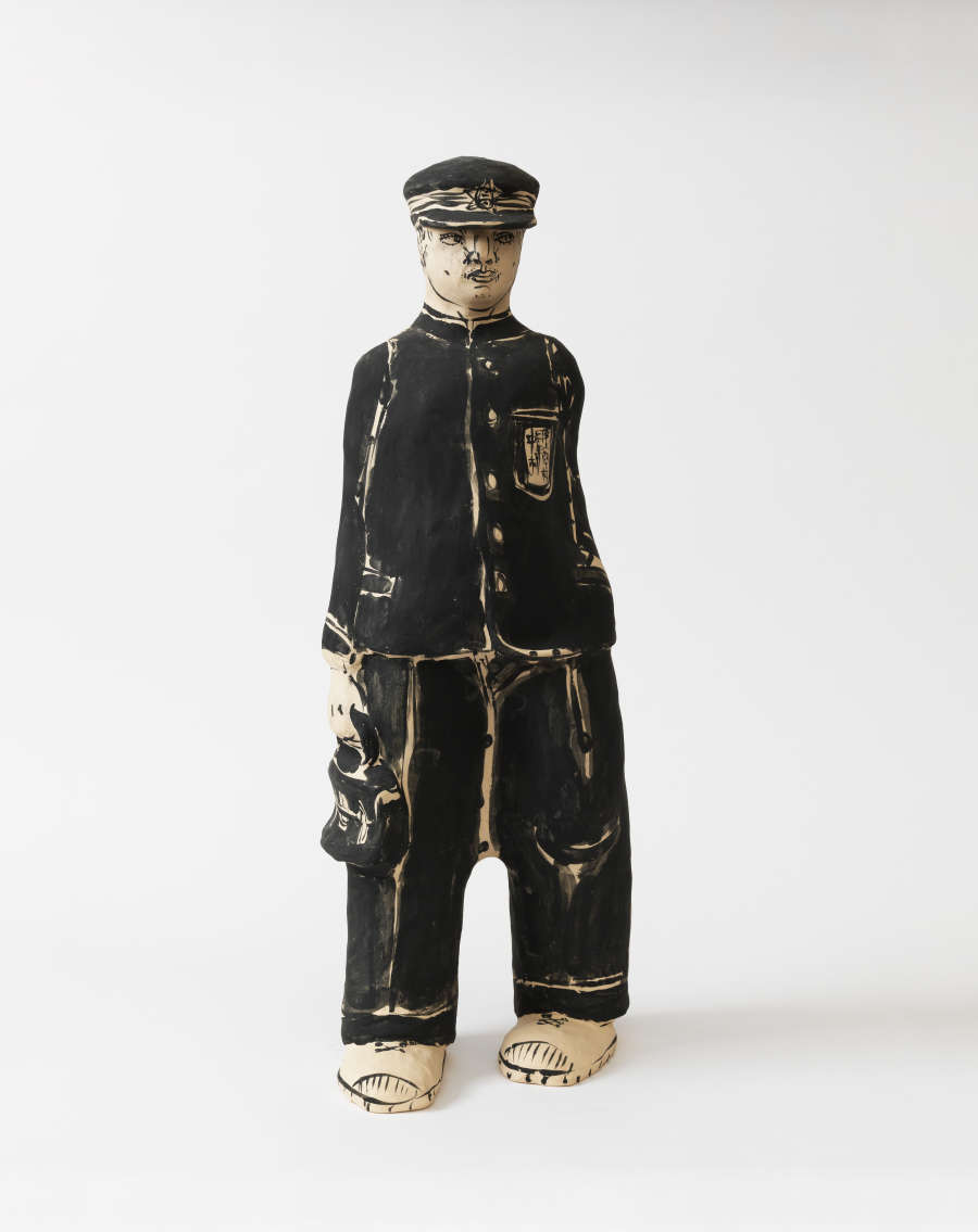 Stylized ceramic figure of a young man in a black uniform and cap, his features outlined with bold strokes, standing upright and carrying a small satchel at his side.