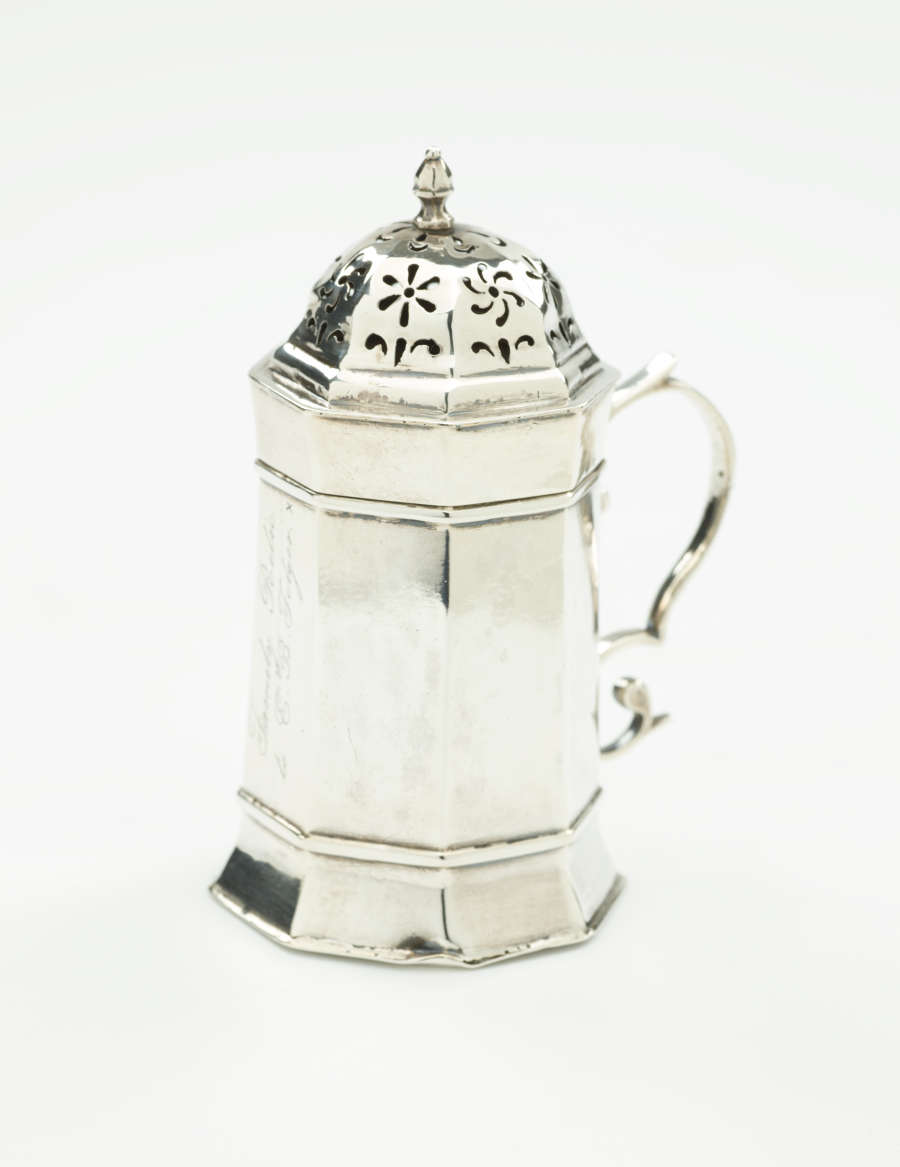  A silver vessel that has an octagonal body, handle, and lid that has floral perforations.
