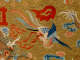 Embroidered textile featuring a vibrant blue, red, and gold phoenix soaring amid multicolored clouds and red flames, set on a gold background.