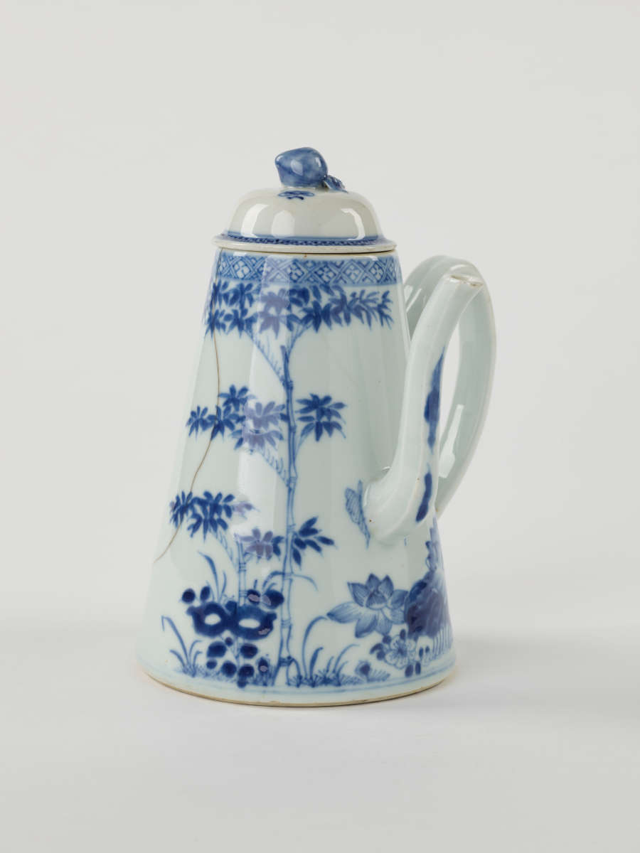 A white and blue teapot with floral decorations, a lid with a small semi spherical finial, spout, and a handle which is located approximately 90 degrees from the spout.