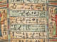 A close-up of a coffin with horizontal bands of black hieroglyphs on faded blue and ochre, framed by a red, blue, and green border.