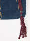 A dark woven textile with golden leaves and a braided red cord extending from the edge in a frayed tassel.