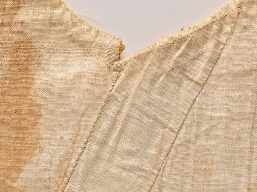 Close-up photo of off-white fabric and seams. At left the fabric is marked with a faint dark stain.