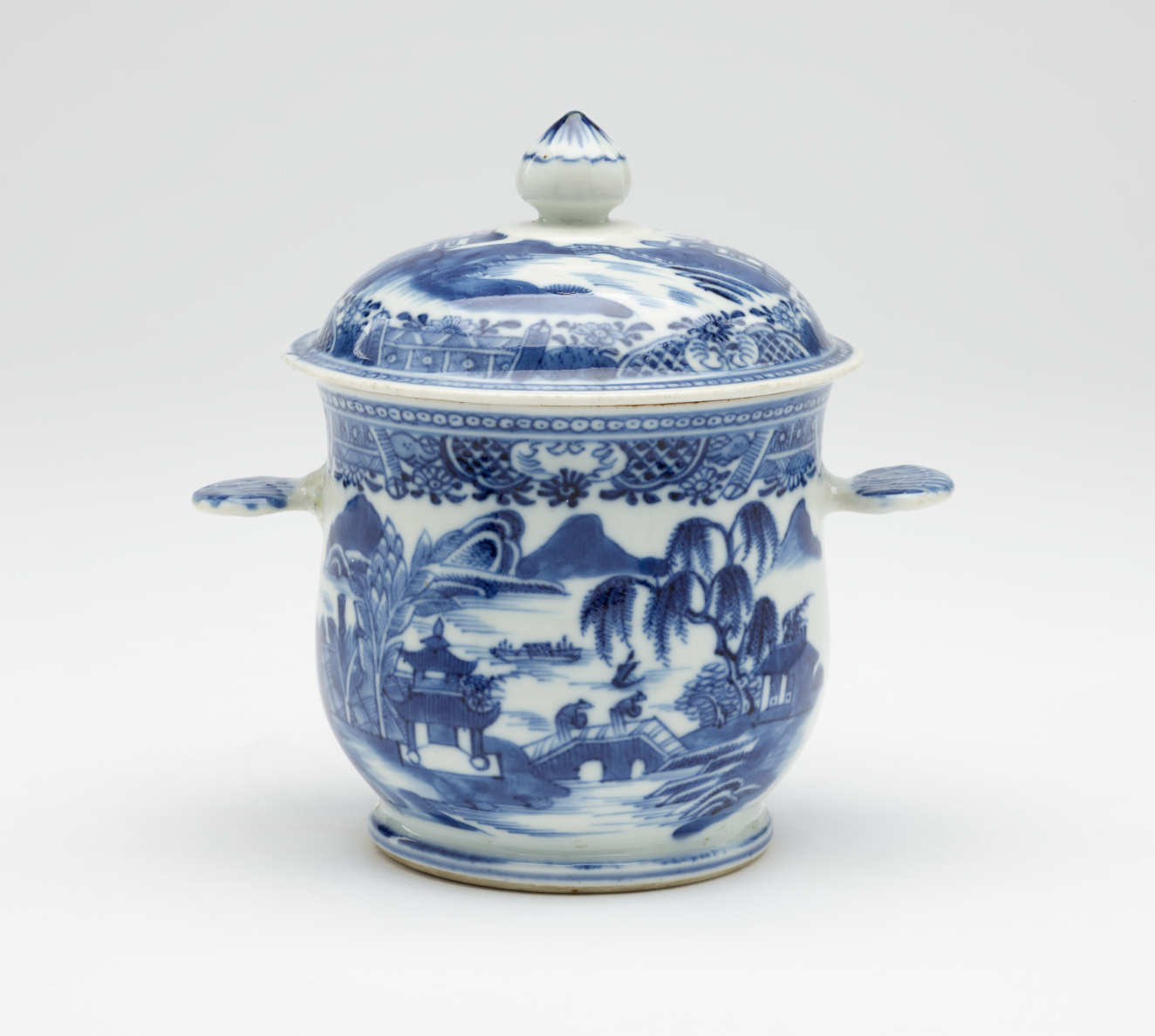 A white bowl with flat handles and lid. The blue decorations are architectural and floral.