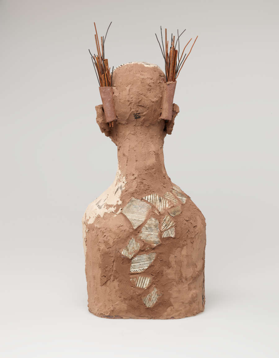 The bust’s back. A line of textured white patches runs down the figure's spine. Two bundles of branches stick out from behind its head. The left shoulder is painted off-white.