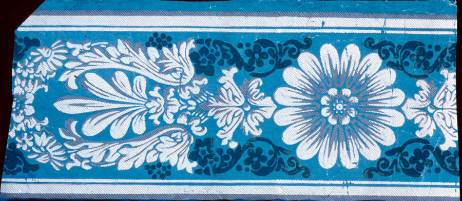 Central white flower surrounded by white and gray floral ornamentation and bordered by white stripes set against a blue background.