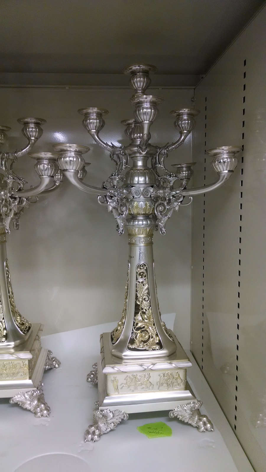 The back view of two of the same candle holders, placed in a storage shelf with white paper underneath them. 