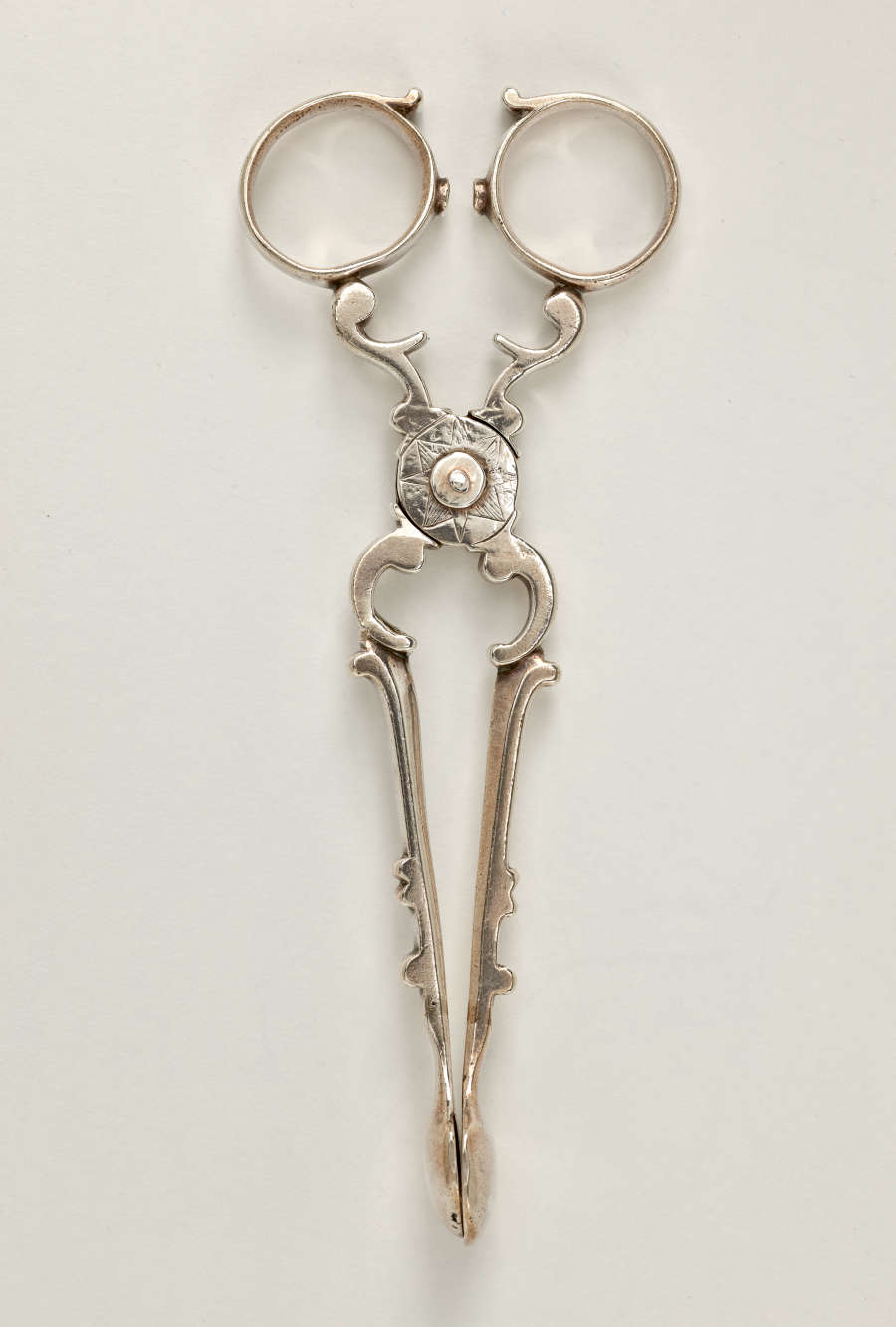Silver sugar tongs that are delicate and swirled.