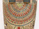 A detailed painted collar on a wooden coffin, featuring repeating patterns of flowers, beads, and triangular shapes in red, blue, and green, framed by hieroglyphic inscriptions and figure illustrations.