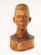 Slightly angled view of a glossy wooden bust depicting the head of a male figure with afrocentric facial features. He has a stern expression and an intense gaze.