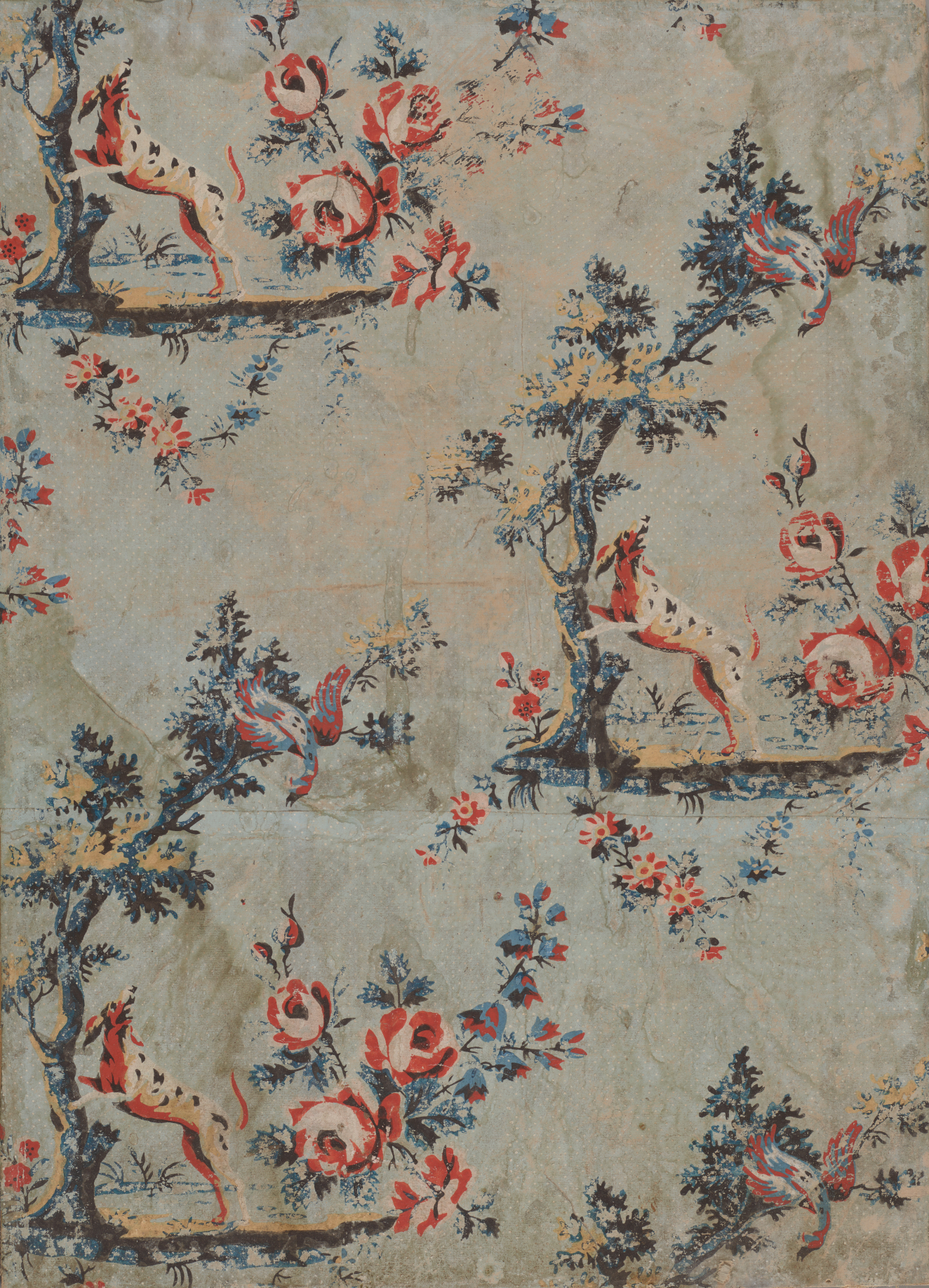 Weathered, light blue wallpaper with repeating motifs of red and pink flowers next to a black-spotted white dog standing on a tree and looking at a bird in the branches.