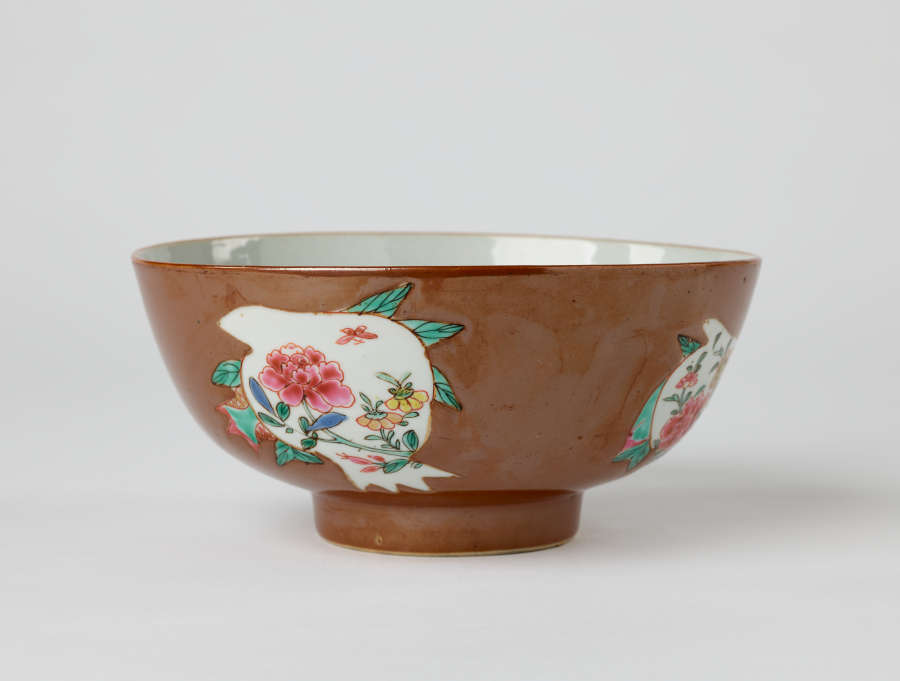 A white and brown bowl with green, yellow, and pink floral decorations with a short, small foot.