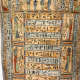 Close-up of a coffin panel with hieroglyphic inscriptions and painted figures in colorful robes.