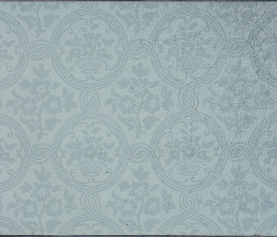 A blue gray segment of wallpaper featuring a faded floral motif design alongside intricate arranged looping curves.