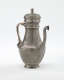 A silver coffee pot with detailed delicate decorations, handle with a lid hinged to it, and spout.