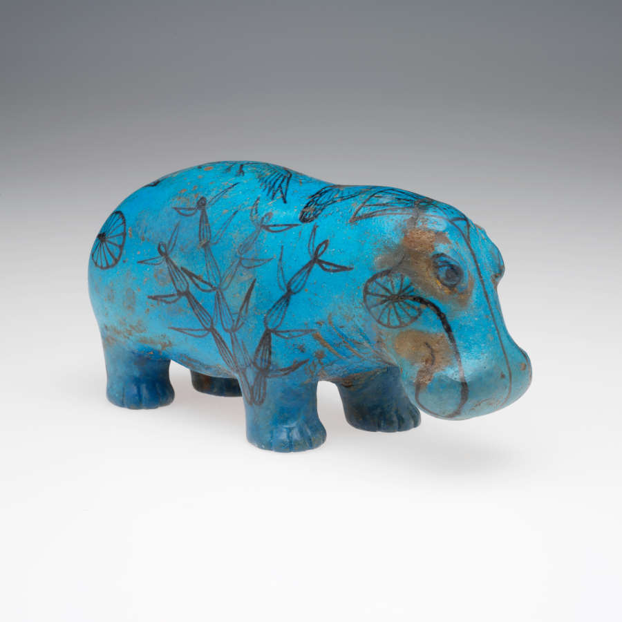 Quarter view of a blue sculpture of a standing hippopotamus with black outlines of birds, insects, plants and waves on its glossy surface. It stands against a gray background.