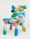 Sculptural chair with intertwined glossy colorful balloon-like shapes arranged in an abstract manner against a stark white backdrop.