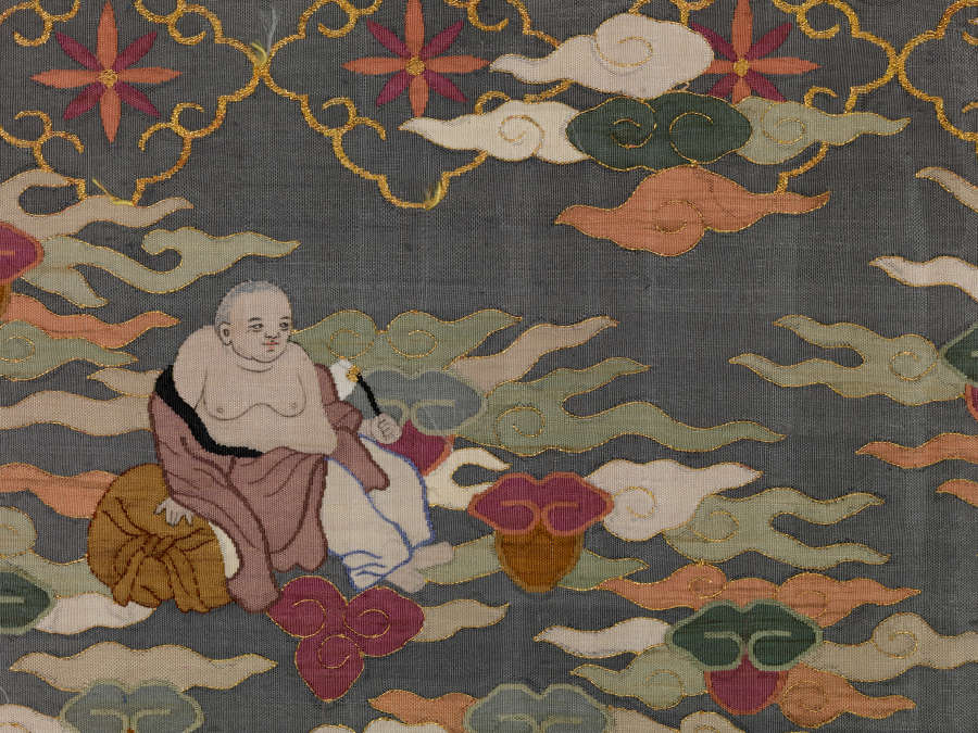 Section of illustrations on the blue-gray robes back, featuring a latticed floral pattern and below, densely-packed pastel wispy clouds. A seated monk in brown robes holds a fly whisk.