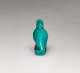 Back of a turquoise amulet, of a crouching pelican-like bird with a long beak pointed downwards, head tucked into its neck, where there is a small loop.