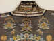 The collar of a richly embroidered garment with gold-threaded designs, multicolored cloud motifs, and mythical creatures. 