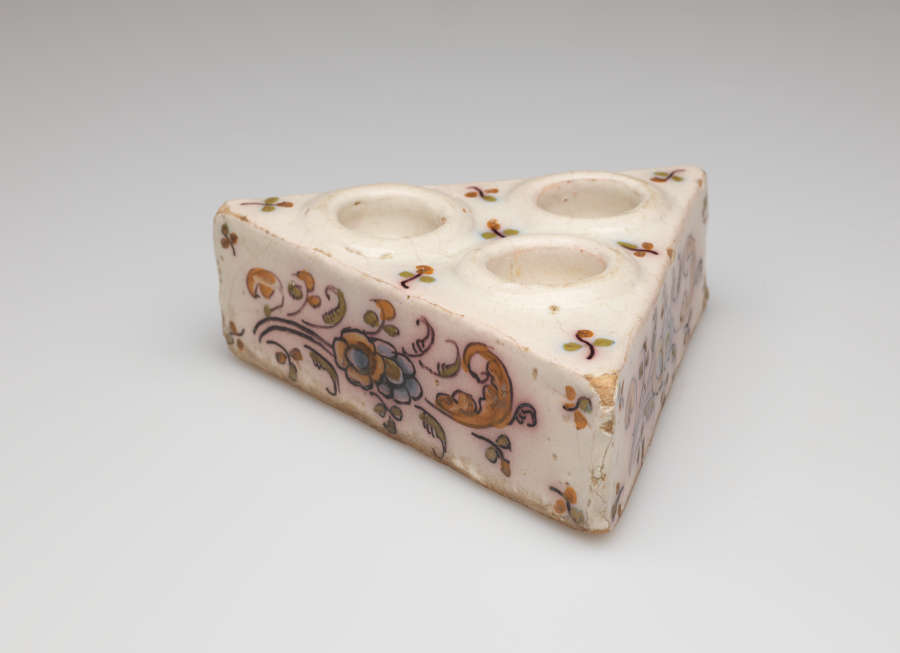 A cream colored triangular salt cellar with three holes on the top with decorative floral decorations.