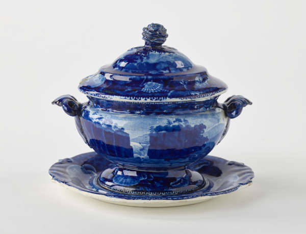  A dark blue decorative sauce boat. Two symmetrical sculptural handles that depict a bird’s head, foot, and lid with rounded finial