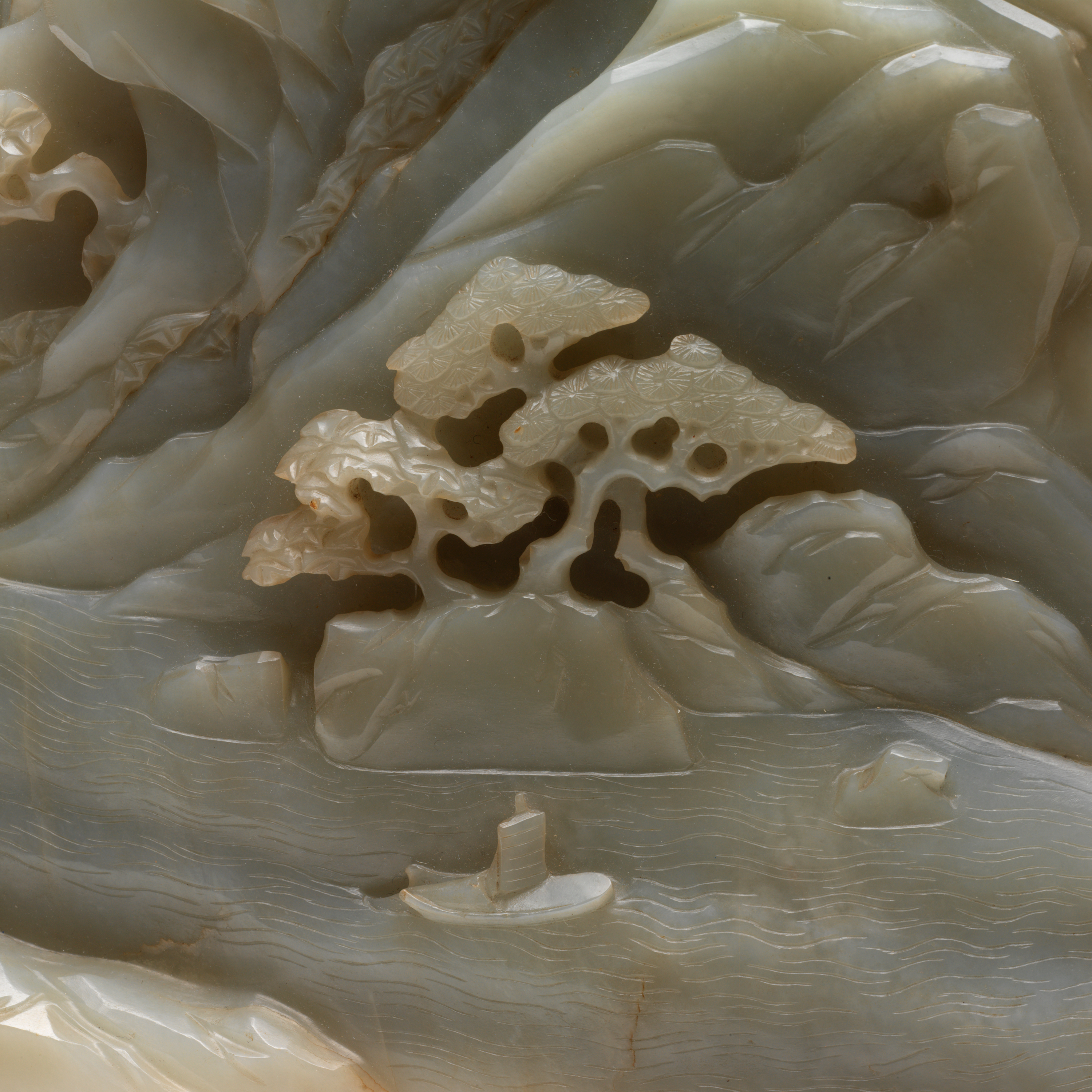 A small, delicate sailboat gliding across water beneath rocky cliffs and detailed trees carved in jade.