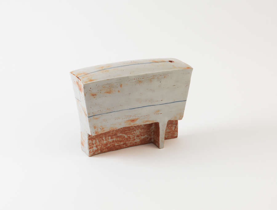 Rectangular ceramic sculpture with a pale, whitewashed surface flecked with rust colored specks, divided by a thin horizontal line above a rough, weathered red-brown base. 