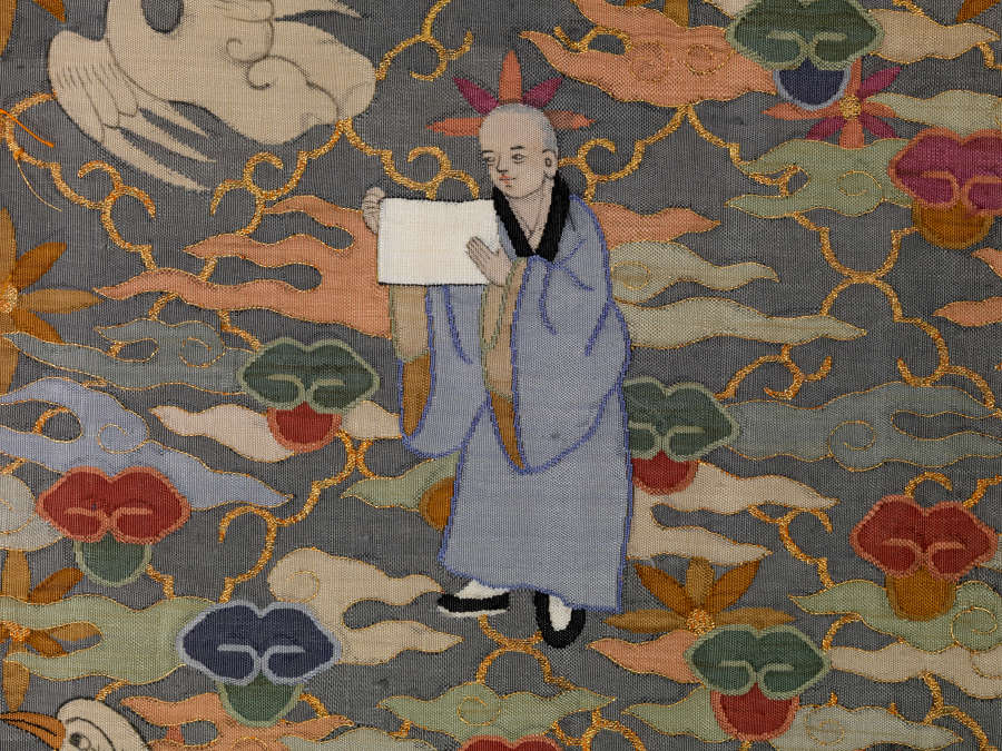 Robe’s back detail, showing a bald monk holding a white sheet of paper, amongst earthy pastel clouds and a flying bird against a gray background with a diagonally running grid.