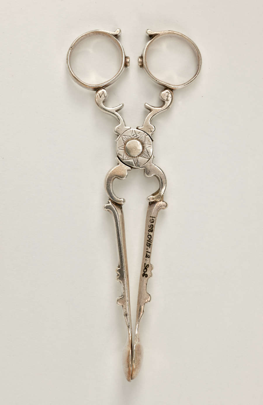 Silver sugar tongs that are delicate and swirled.