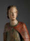 A weathered wooden statue of a figure with a solemn expression, with red and green drapery.