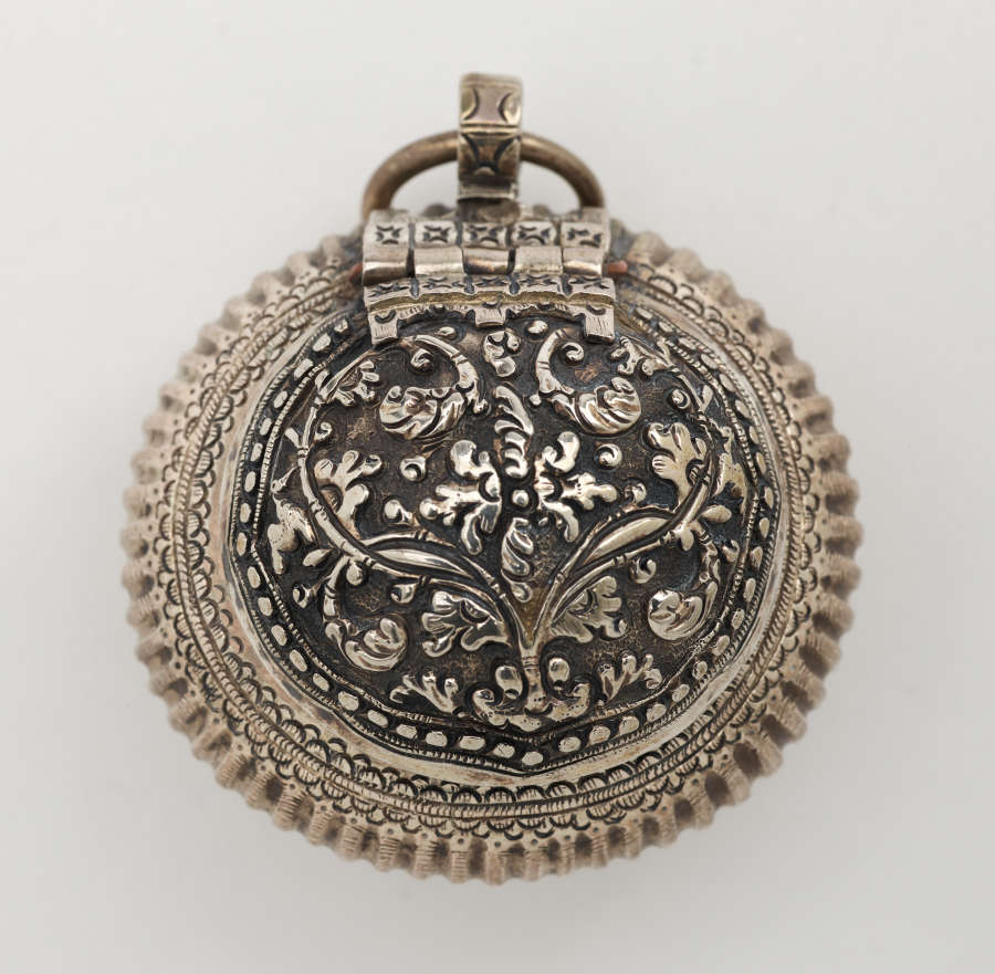 Rounded metal container with raised floral designs. A small circular metal ring attached to the top.