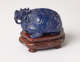 A side view of a blue sculpture of a horned tortoise, whose surface is covered with carved geometric patterns. It stands on a brown base with steps and golden patterning.