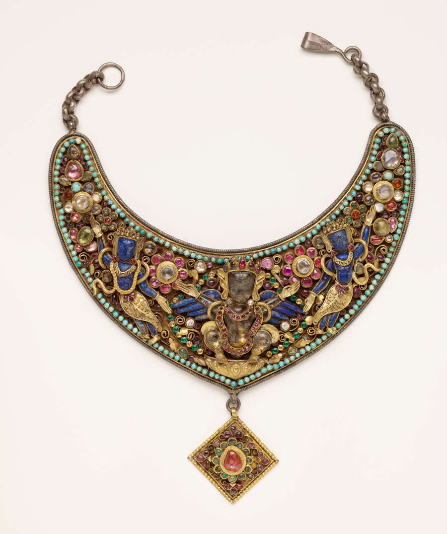 An ornate crescent necklace and gold diamond-shaped pendant, featuring a symmetrical flowing arrangement of green, blue, pink, and golden floral motifs and figures in precious metals, stones and beads.