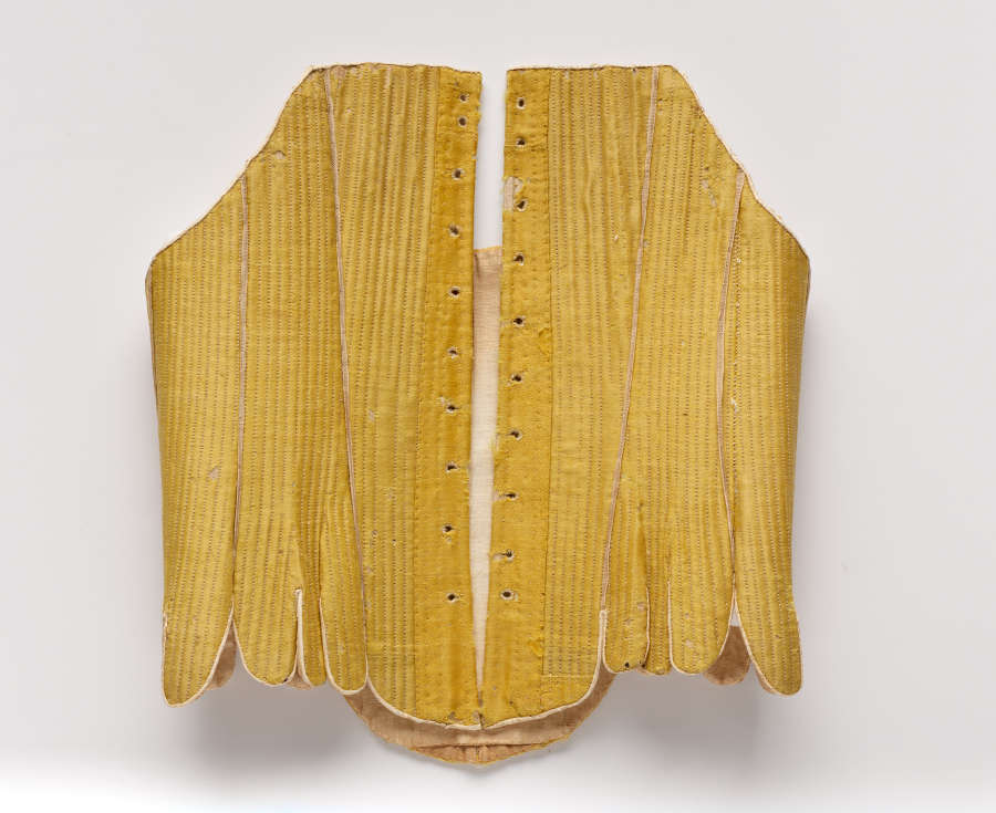 Photo of the front of a stitched gold-colored garment. Iit is open in the front and scalloped at the bottom.