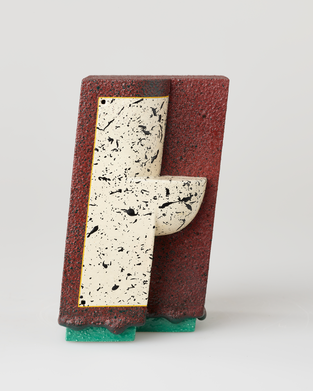A slanted rust red rectangle with a rough grainy surface with an embedded white speckled panel and rounded protrusion supported by a green base.