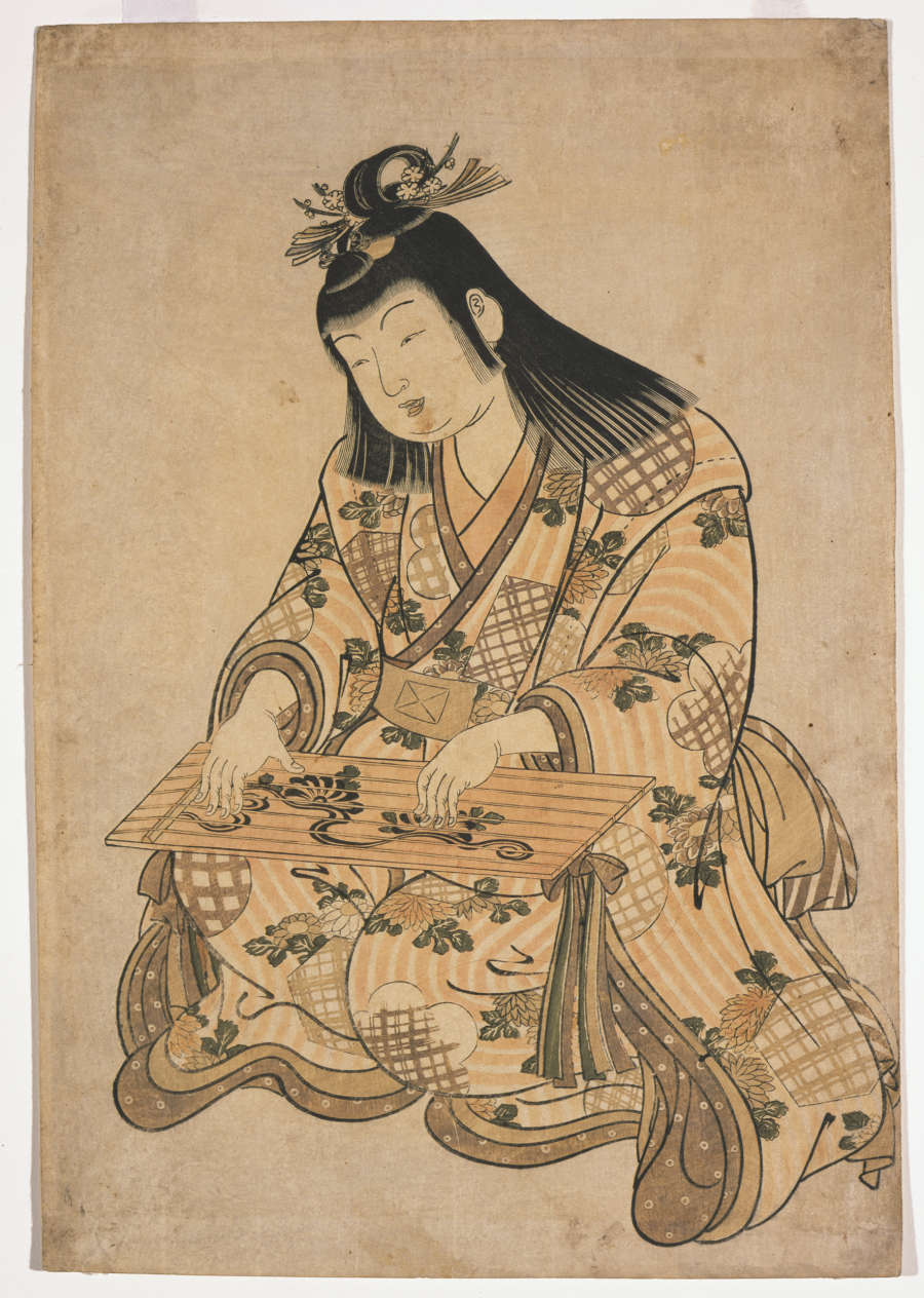 A polychrome woodblock print in muted tones. A seated child in a chrysanthemum-patterned long-sleeved robe plays a toy zither.