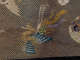 A multicolored mythical bird with ornate outstretched wings and swirling feathers set against a gold mesh background.