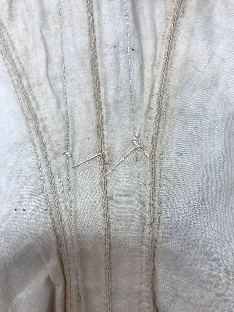 Close-up of aged cream fabric with visible stitching curving lines and an imperfect thread knot at the center. 