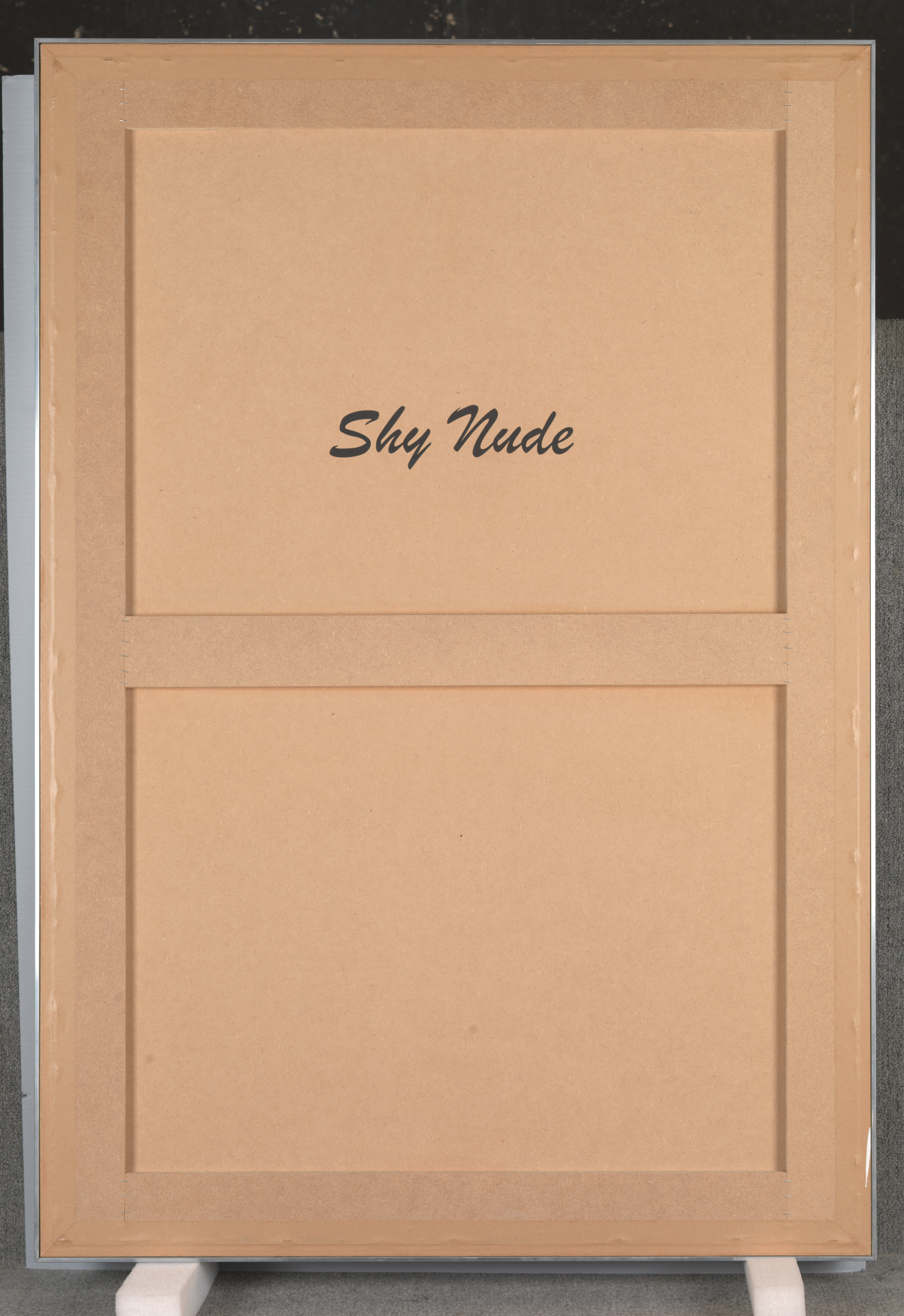 Back of a framed panel leaning against a corner, with the label "Shy Nude" in large print in a cursive font.