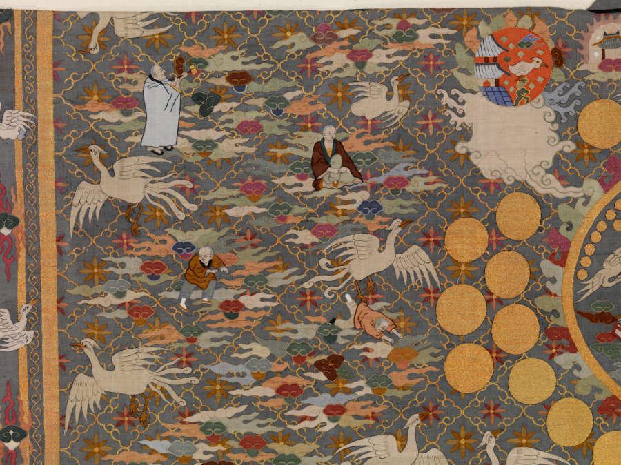 Detail of the top-left quarter of the robe’s back, featuring densely-packed illustrations of white birds, earthy-pastel clouds, robed priests, golden circles and floral motifs against a background of layered patterns.