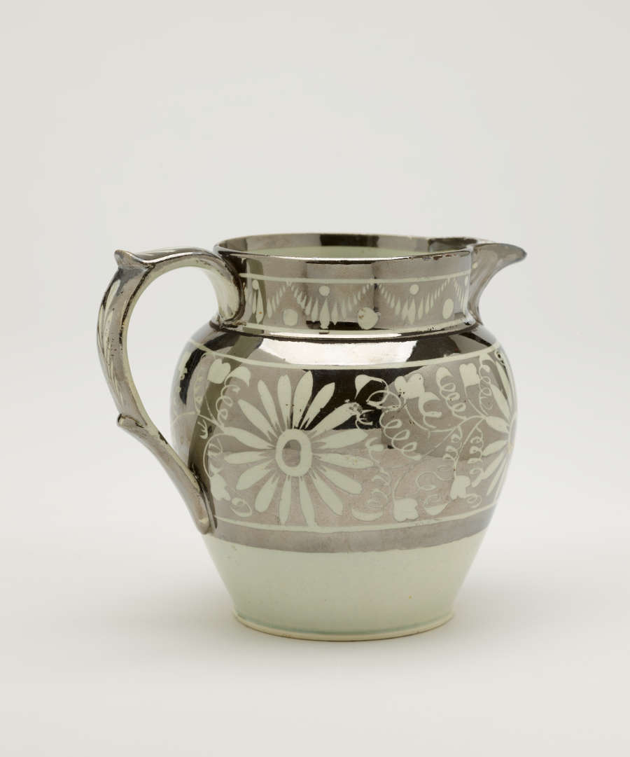 A silver-colored jug with floral motifs on the body of the vessel.