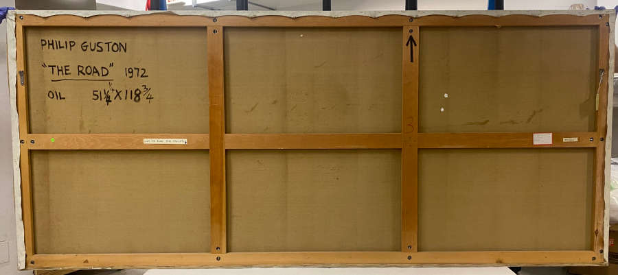 Large canvas framed by wooden crossbars, reading “Philip Guston, ‘The Road,’ 1972”  handwritten in black on the upper left, with several small white labels attached.
