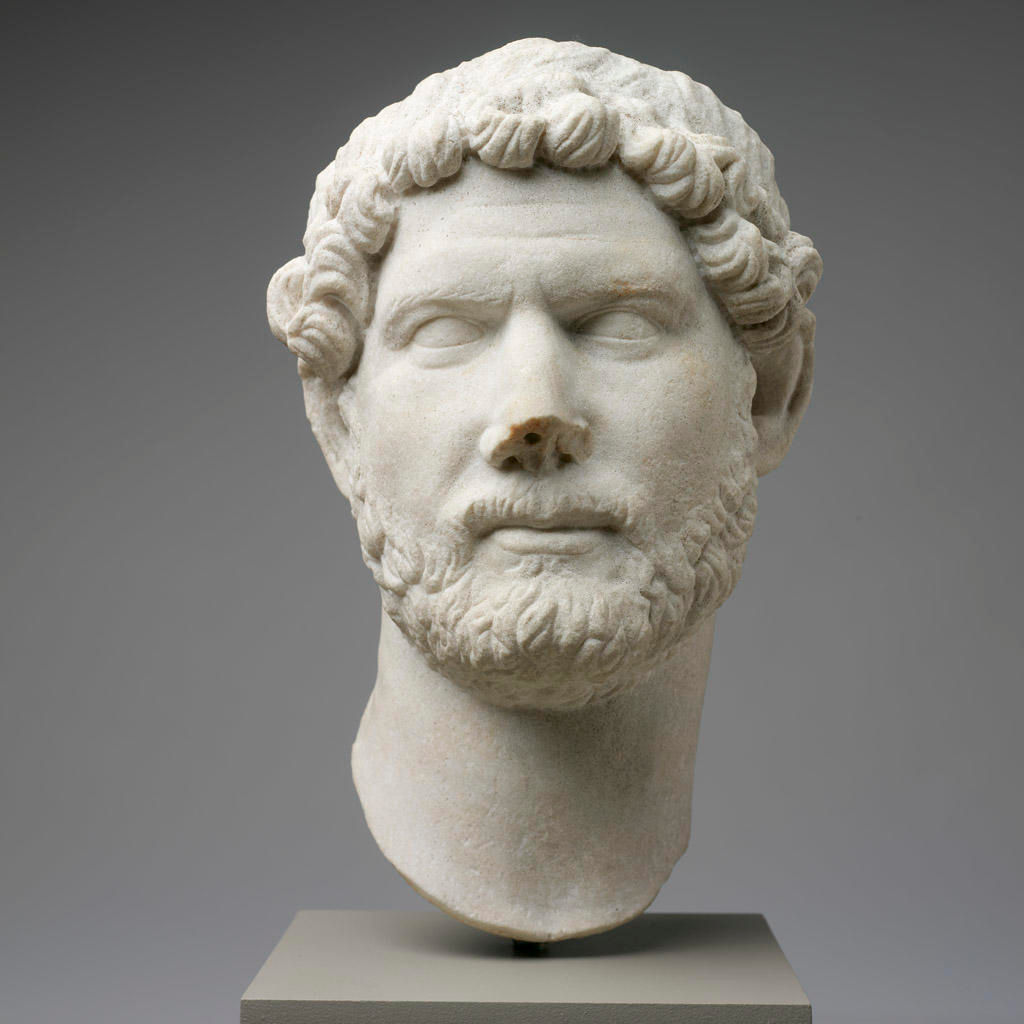 Marble bust of a bearded man with realistic carved facial details. The head is centered on a gray backdrop and cut off below the chin and above the eyes.