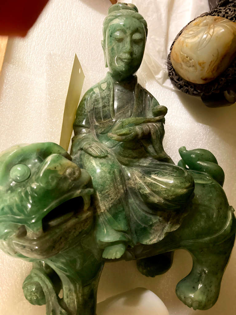 View in storage of a green and brown glossy sculpture of a robed man, eyes closed, seated on a lion with short legs and a large face and open mouth. 