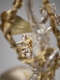 The backside of a silver cherub with curly hair, small gold feathered wings and robes in sharp focus behind a blurred silver figure in the foreground. 