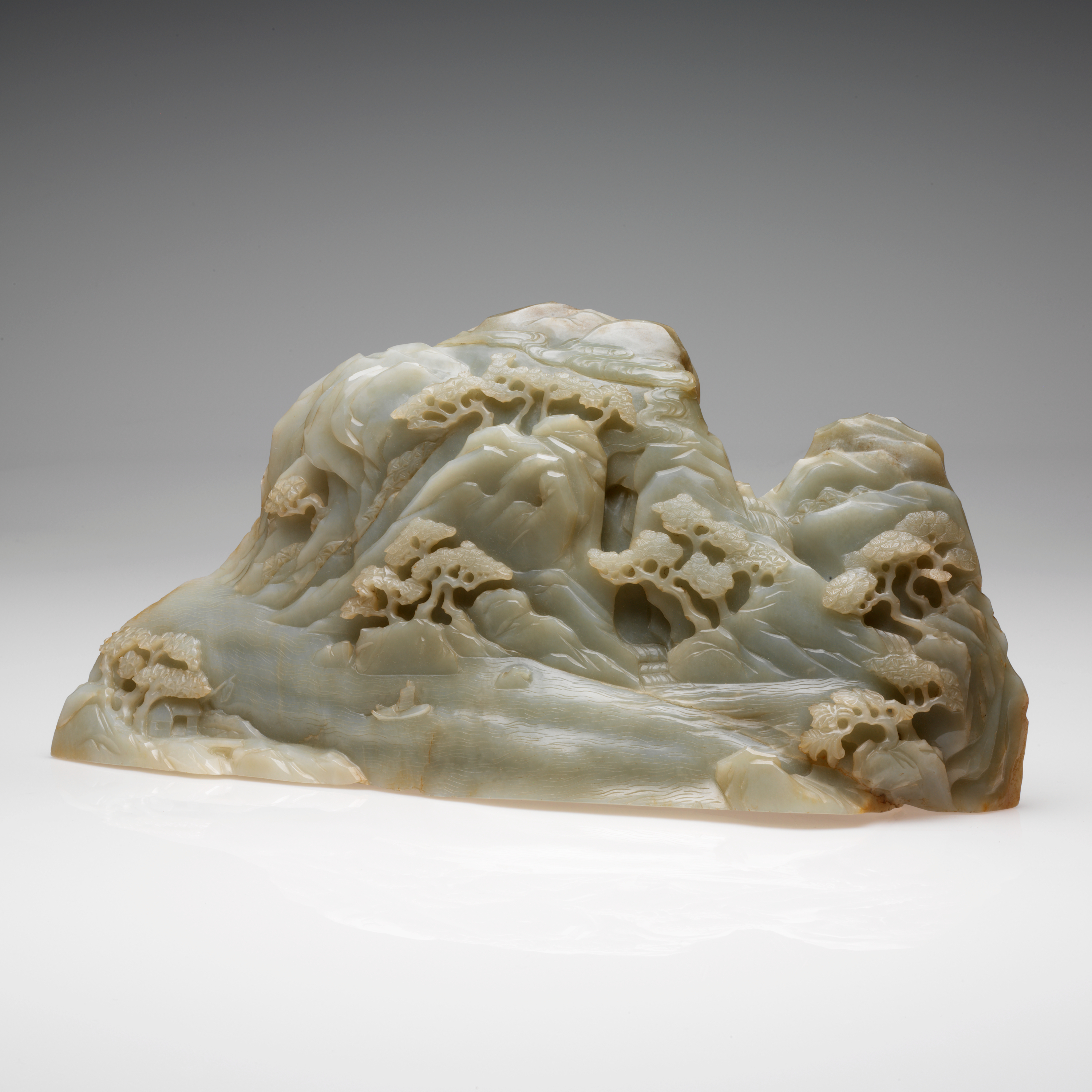 A pale green, smooth jade carving resembling mountain peaks dotted with clustered tree and a small waterfall in the center. 