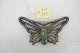 Silver butterfly pin against a white background. An inlaid rectangular gold-speckled piece of jade makes up the body. Above it is a small cream tag that reads “67.173”